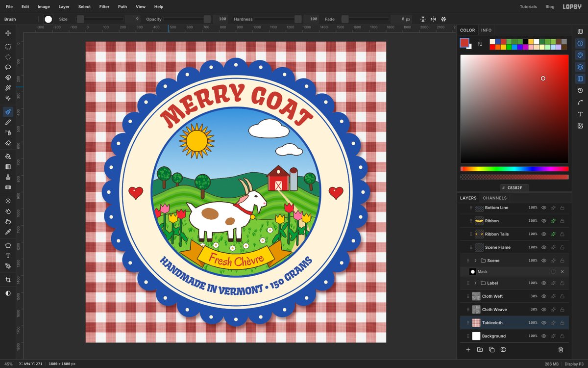 Lopsy showing the finished Merry Goat cheese label, a scalloped cobalt sticker with an arched red title, a painted goat in a meadow with a red barn, tulips and a yellow Fresh Chèvre ribbon, lying on a red gingham tablecloth